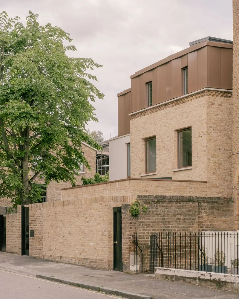 Street view of the buff brick facade with copper-panel extension rising above under overcast skies