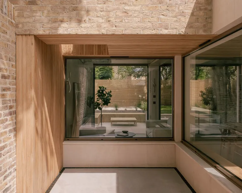 Timber-lined bay window overlooking internal courtyard framed by brick wall and concrete structure