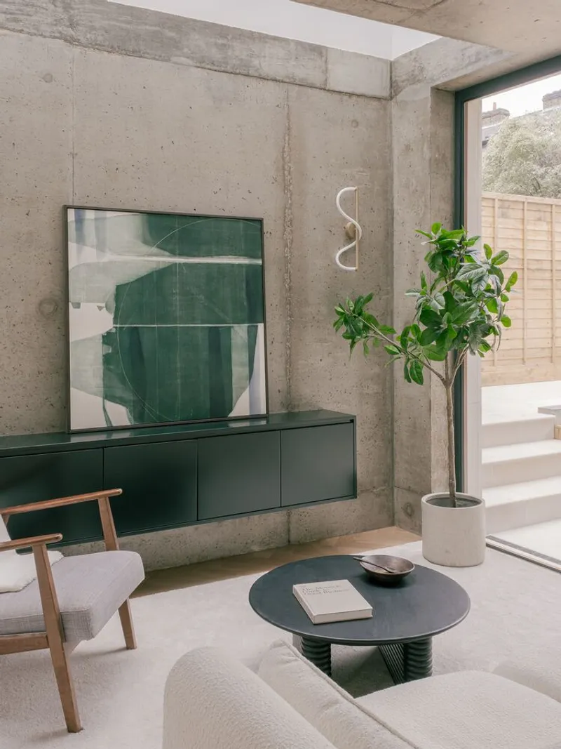 Living room with green media console against exposed concrete walls and potted plant by window