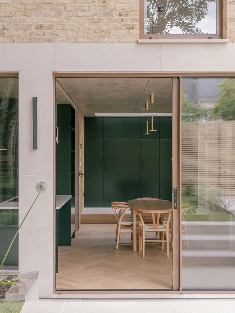 Open sliding glass door revealing dining area with green cabinetry and exposed concrete ceiling