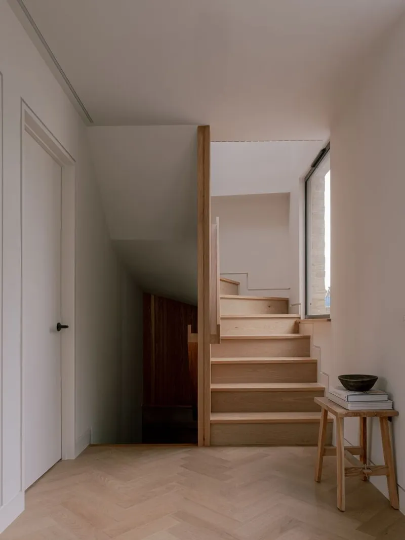Timber staircase with open risers beside narrow window in white painted hallway