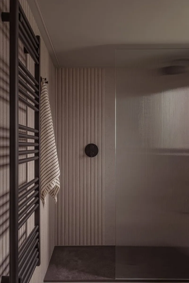 Bathroom corner with vertical timber slat wall, black towel radiator and frosted glass shower partition