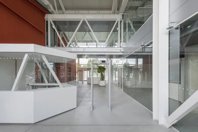 White steel bridge connecting upper levels across polished concrete entry hall with glass and metal facades