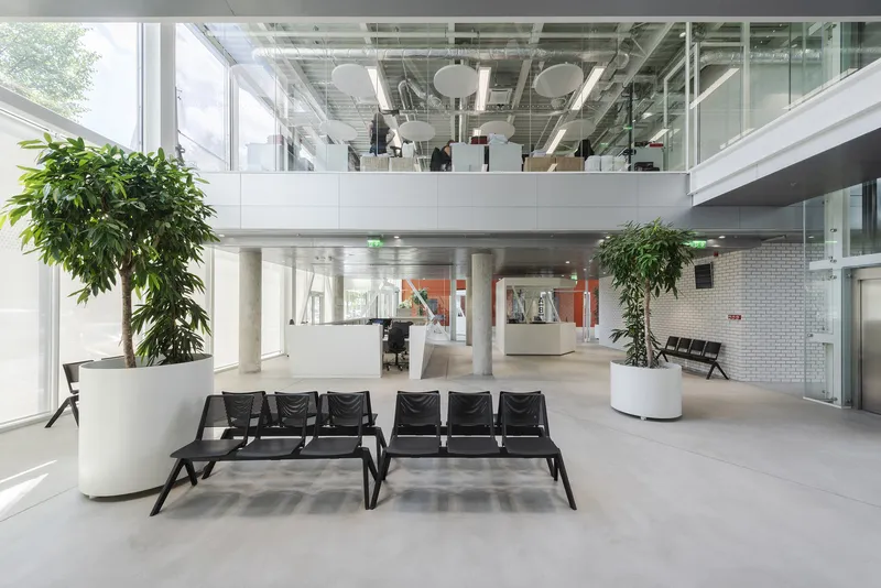 Double-height atrium with exposed mezzanine, black lounge seating, and large planters in white pots