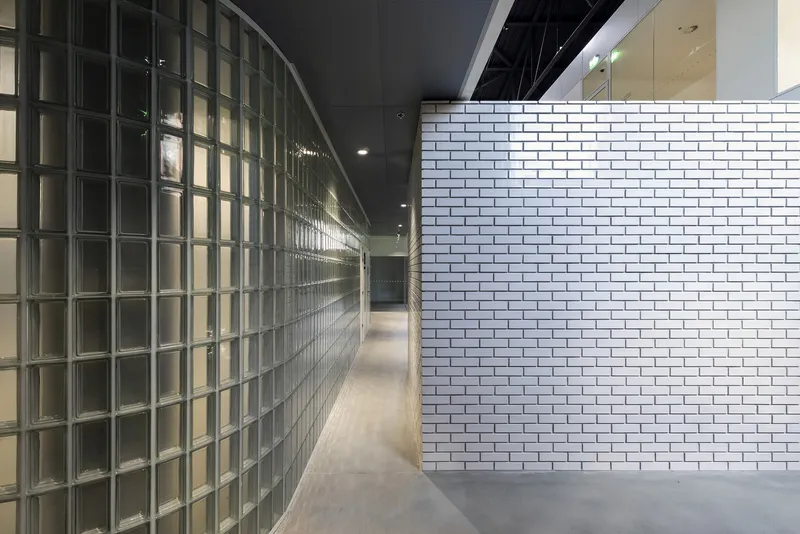 Interior corridor with curved glass block wall opposite white subway tile partition under black ceiling