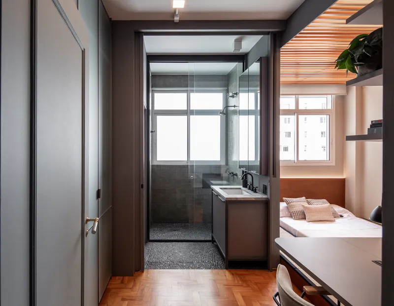 View through bedroom into compact bathroom with dark tile and glass shower enclosure