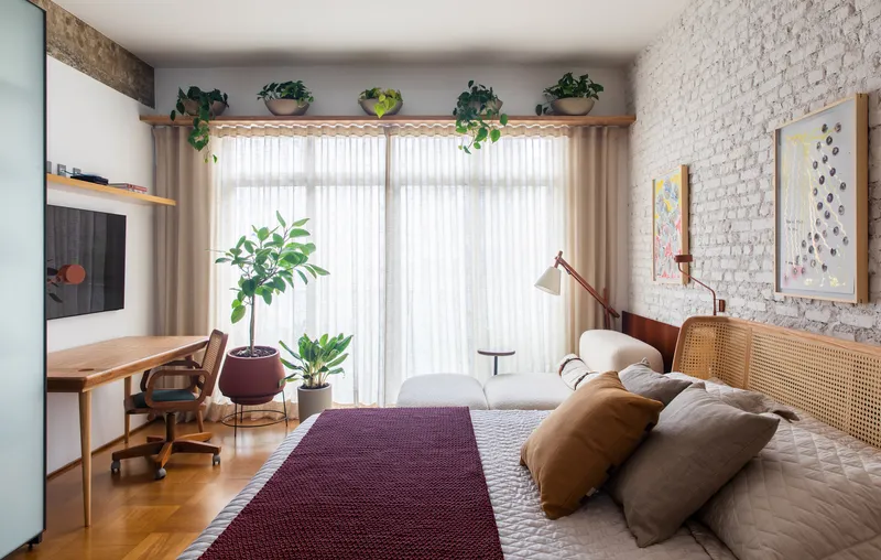 Bedroom with painted white brick wall, sheer curtains and potted plants on parquet floor
