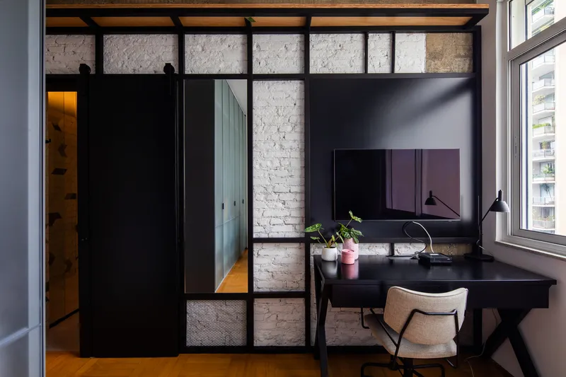 Black sliding barn door and steel-framed glass partition alongside a desk with white brick wall beyond