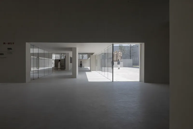 Gallery space looking through glass doors toward exterior courtyard with visitors walking in sunlight