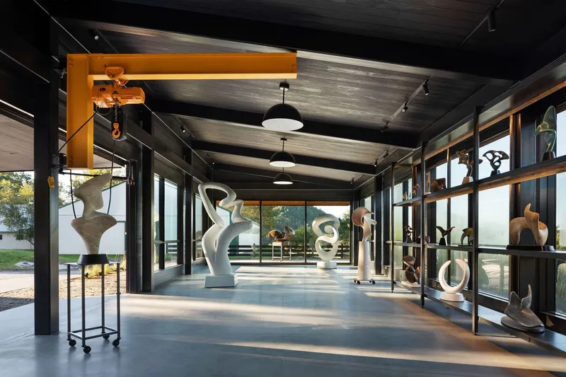 Gallery corridor with exposed timber ceiling, pendant lights, and sculptures displayed on stands and glass shelving