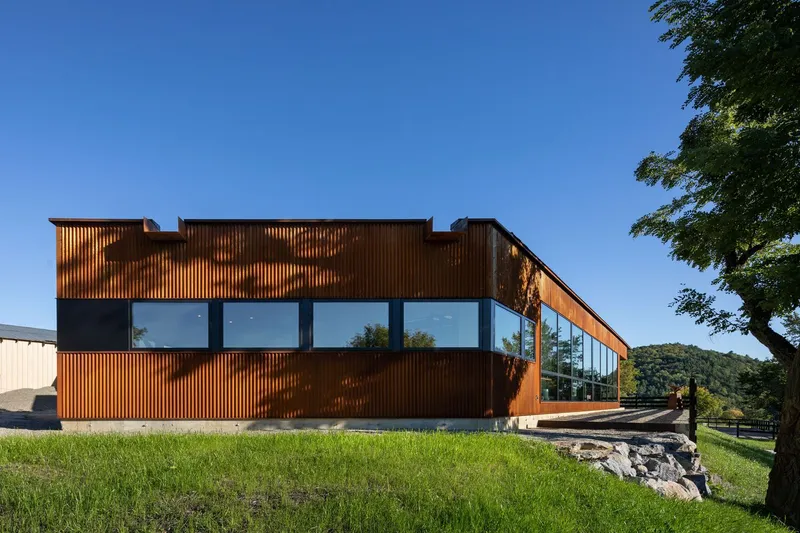 Weathered copper cladding and continuous glazing facade overlooking a grass lawn and stone retaining wall