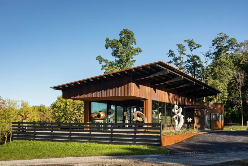 Entry facade with deep roof overhang, horizontal slat fencing, and sculptural artworks visible through glass