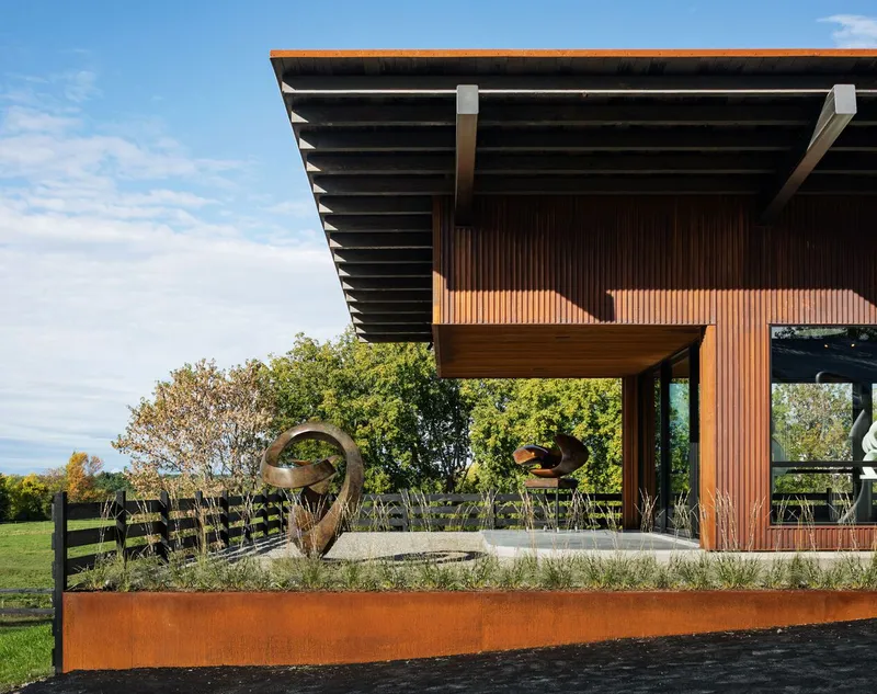 Vertical timber cladding and deep cantilevered roof over a planted bed with weathering steel edge and sculpture