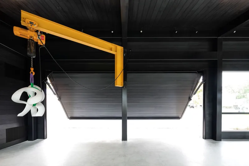 Garage interior with yellow overhead crane and two lifting sectional doors beneath a black slatted ceiling