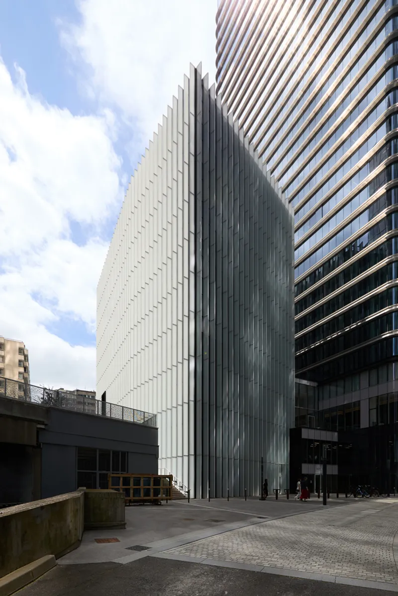 Vertical metal fin facade rising above the street level entrance under a cloudy sky