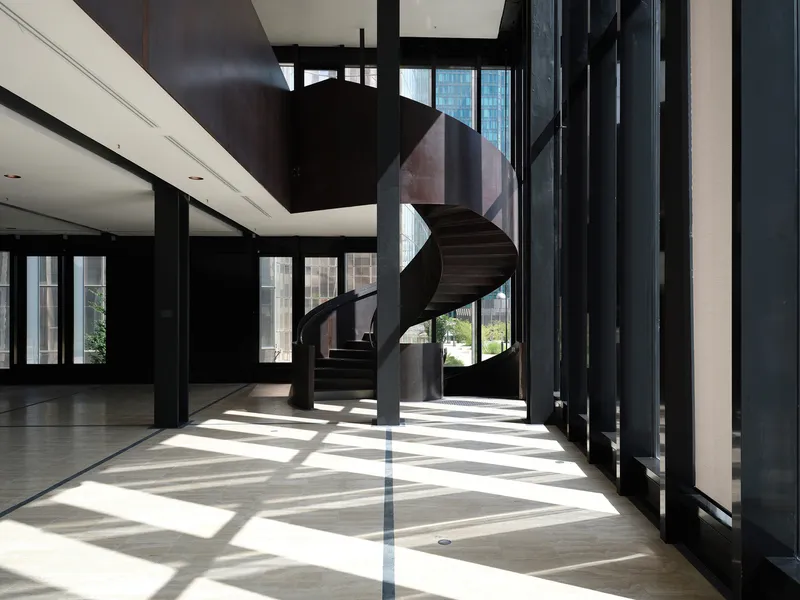 Interior lobby with spiraling staircase and sunlight striping the polished floor through vertical black screens