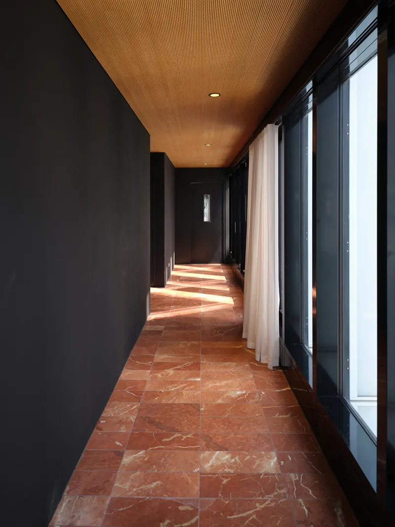 Corridor with red marble tile floor and timber slat ceiling casting afternoon shadows through glazed walls