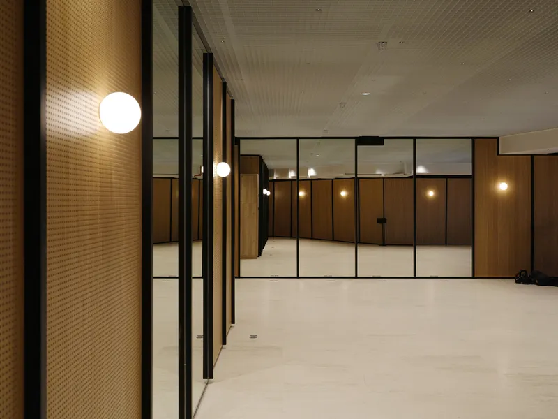 Evening view of lobby space with textured wall panels and black-framed glass partitions under perforated ceiling