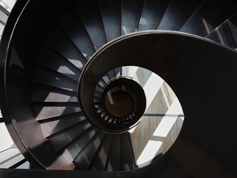 Top-down view of the spiral staircase with dark steel treads and sunlight illuminating the central void