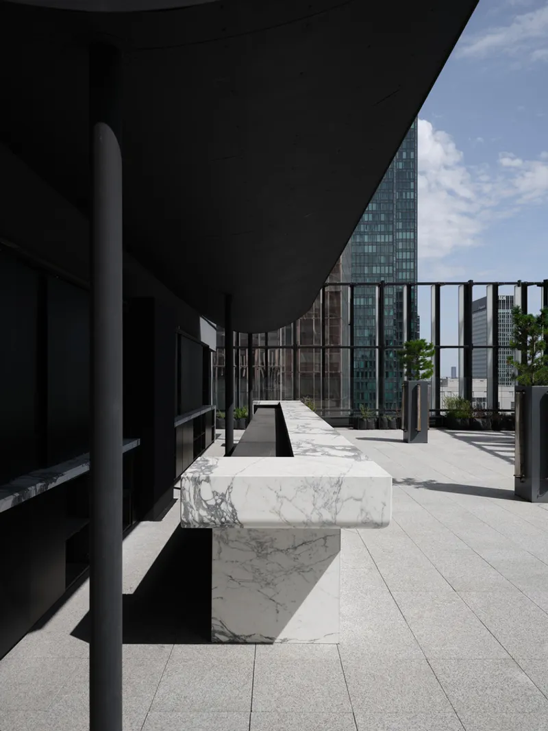 Rooftop terrace with white marble benches and black metal railing framing glass towers beyond