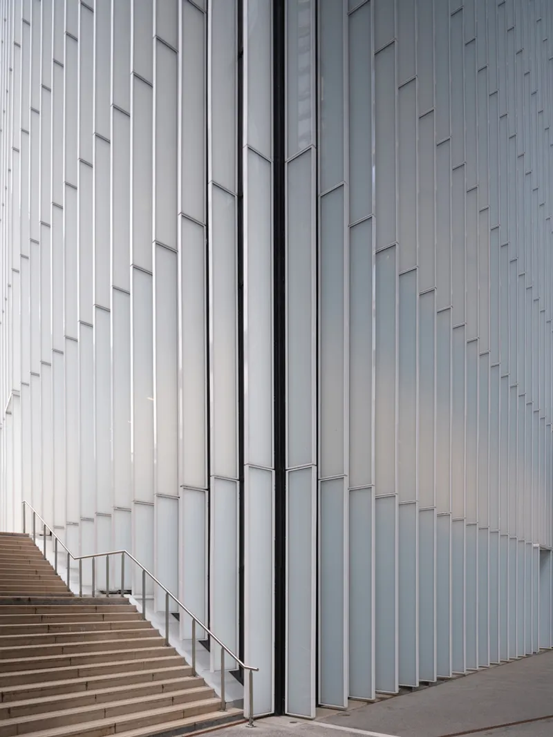 Corner detail of vertical metal fins wrapping the facade beside an exterior stair with handrail