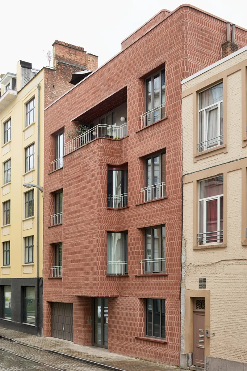 Red brick facade with recessed balconies and windows between neighboring masonry buildings on a cobblestone street