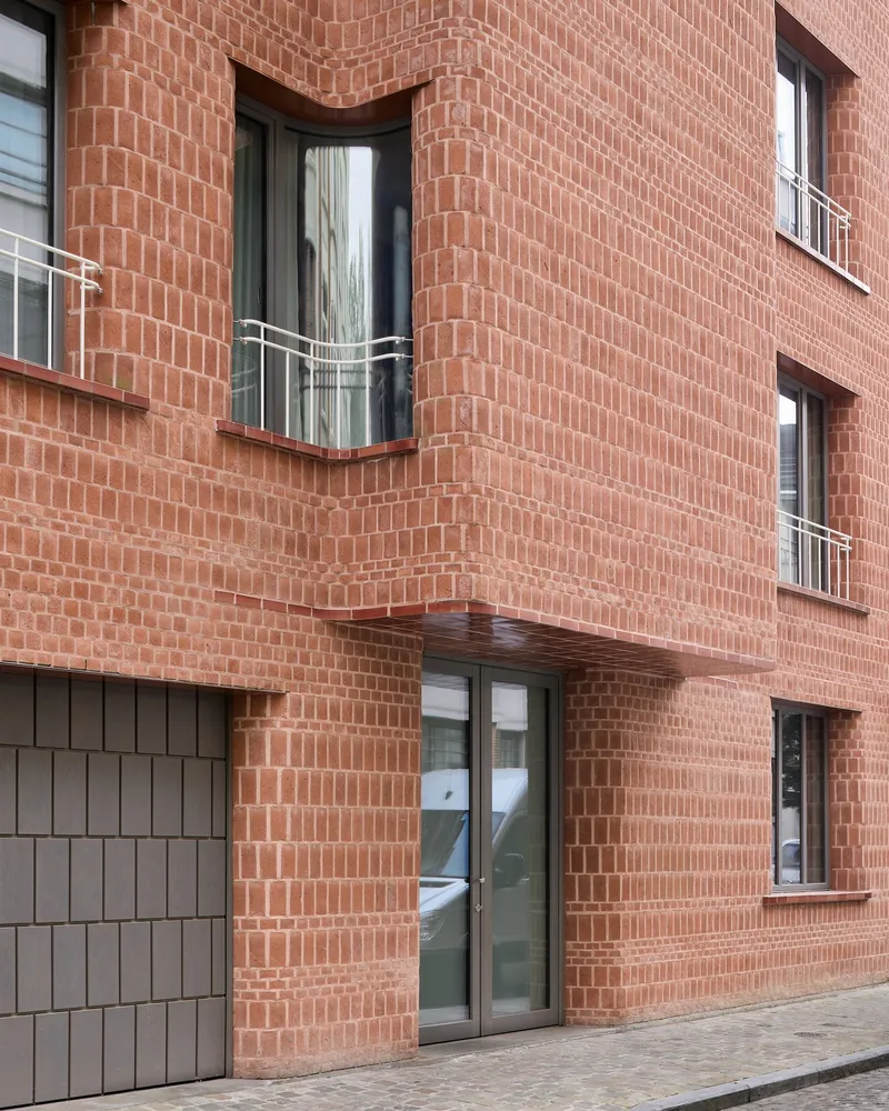 Close-up of curved red brick facade showing recessed balconies and windows with metal railings