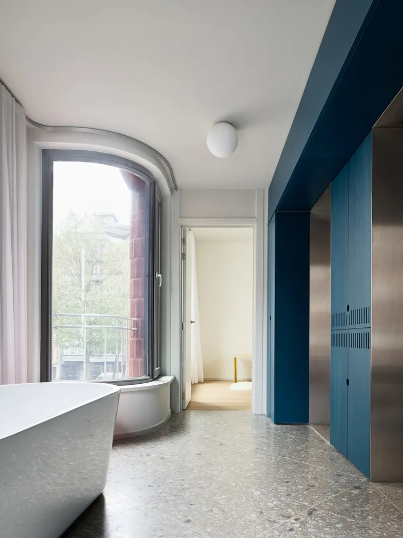 Interior room with freestanding bathtub beside arched window and blue cabinetry along terrazzo floor