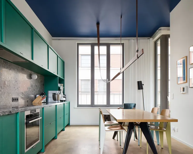 Kitchen with green cabinetry and dining table under a deep blue ceiling and suspended light fixture