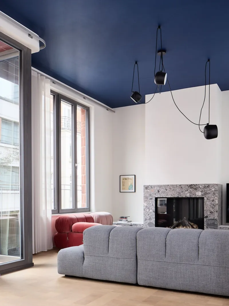 Living room with fireplace set in terrazzo surround beneath a deep blue ceiling and pendant lights