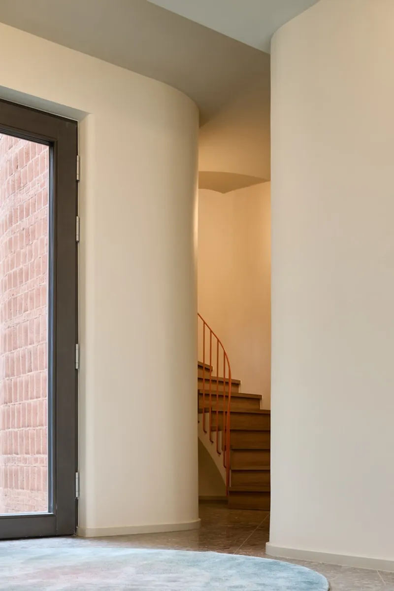 Interior corner with curved plaster walls and wooden staircase glimpsed beyond a glazed door