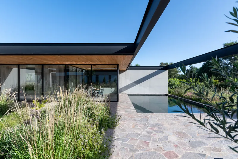 Stone-paved terrace with planted beds extending toward pool deck under cantilevered roof planes