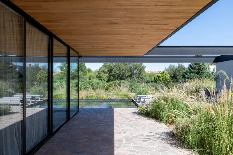 Covered terrace with timber ceiling and glazed wall overlooking pool and grassy landscape beyond