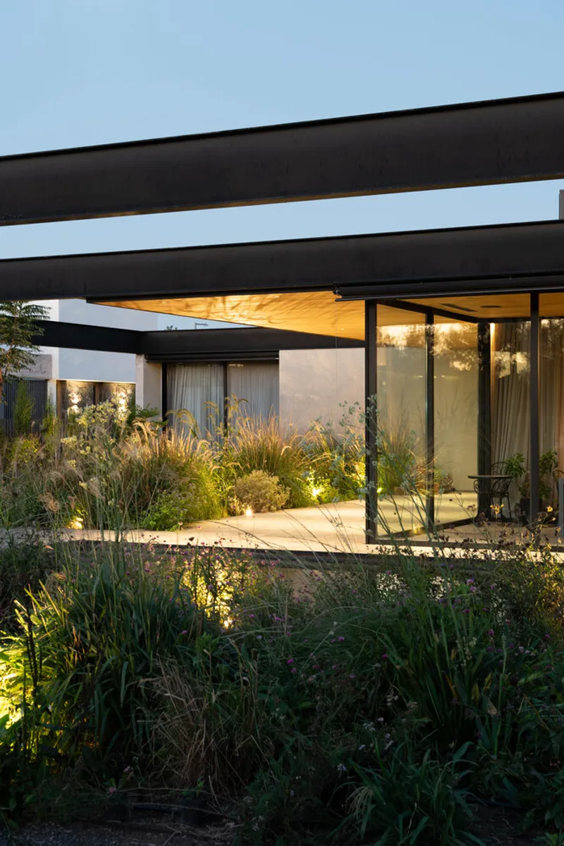 Garden courtyard with steel beam pergola and floor-to-ceiling glazing at twilight