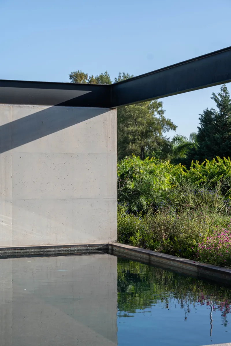 Corner detail of concrete wall meeting steel beams above a reflecting pool