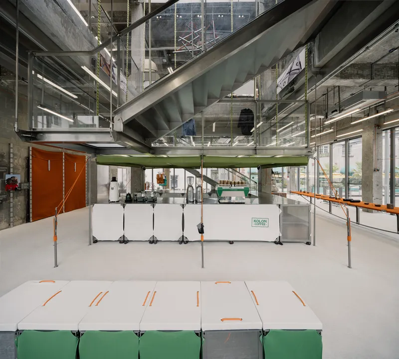 Double-height atrium showing concrete stairs, green platform and white exhibit tables below exposed mechanical systems