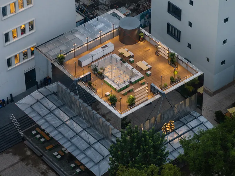 Rooftop terrace with timber decking, planted beds and metal pergola illuminated at twilight