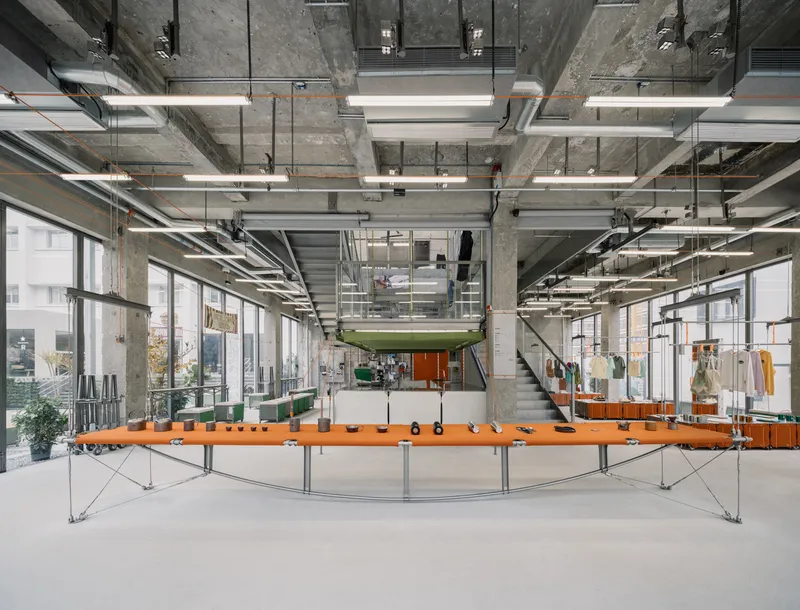 Exposed concrete interior with orange curved workbench and suspended linear lighting fixtures
