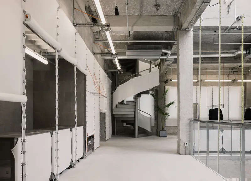 Black steel spiral staircase beneath exposed ductwork and concrete columns in a raw retail interior