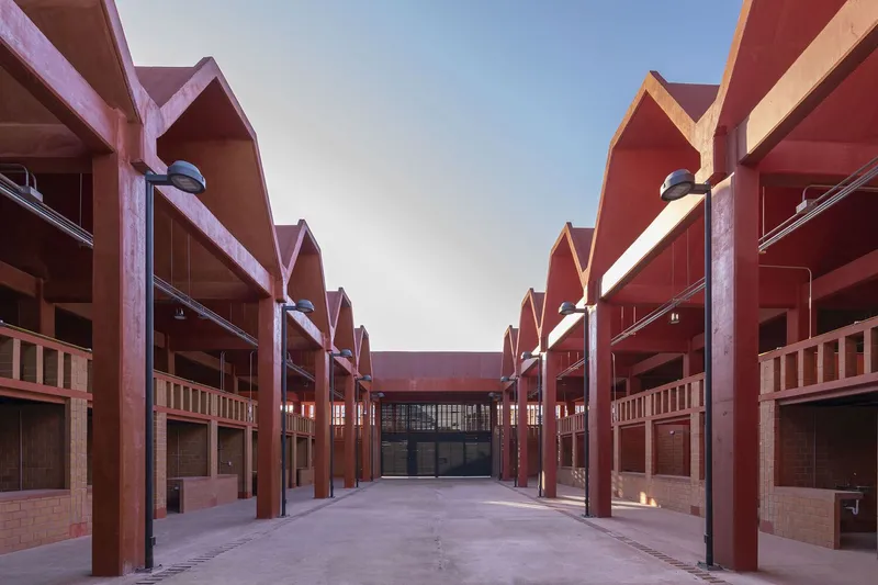 Central courtyard flanked by repeating gabled roofs with exposed steel columns and brick storefronts at dusk