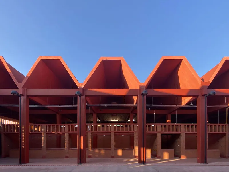 Repeating pentagonal roof forms with glazing below and steel structural frame at golden hour
