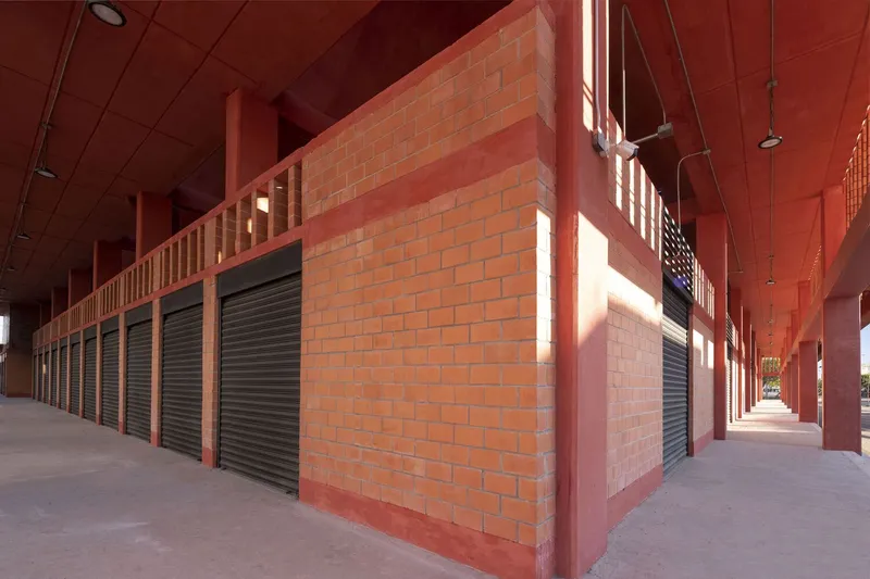 Covered corridor with brick wall and roller shutters casting sharp shadows under painted ceiling