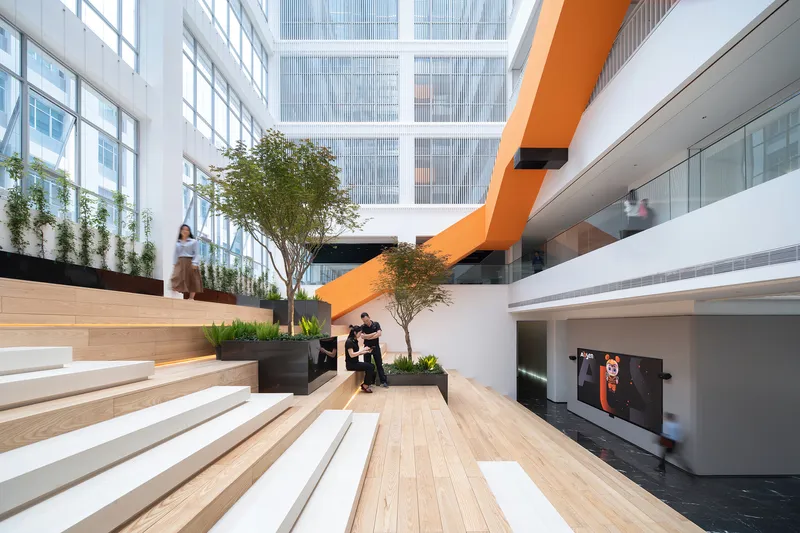 Interior atrium with timber bleacher seating, orange bridge, planters and people gathering in the space
