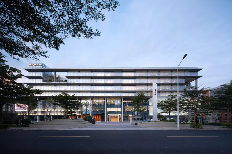 Street view of the horizontally banded glass and panel facade framed by roadside trees at dusk