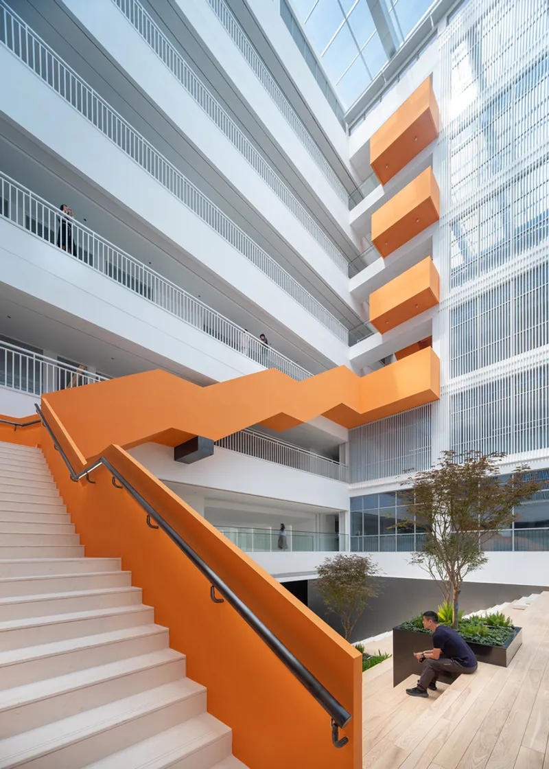 Orange zigzag staircase descending into a courtyard with planted trees and a person crouching near a planter