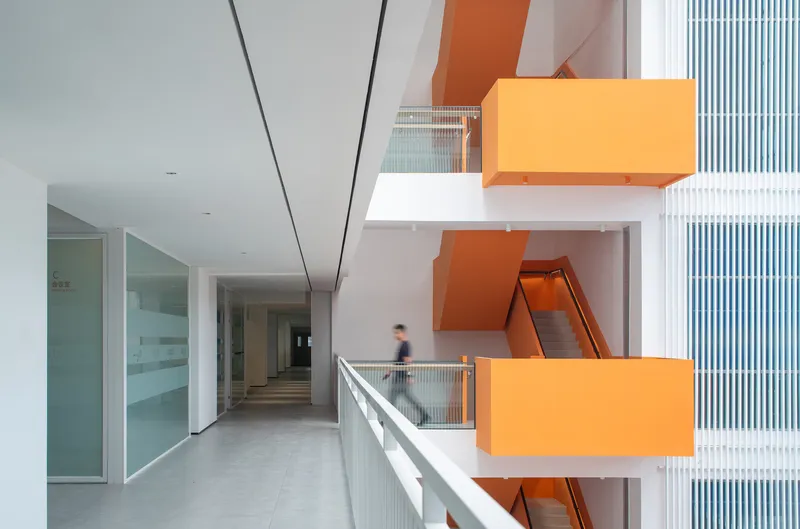 Interior corridor with orange zigzag stair volumes projecting through white balconies and a person walking