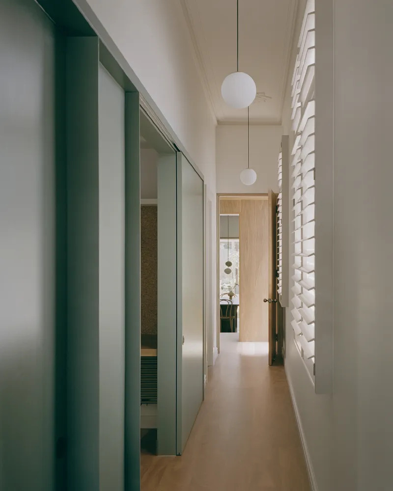 Narrow corridor with green sliding doors and globe pendants beside a perforated screen wall