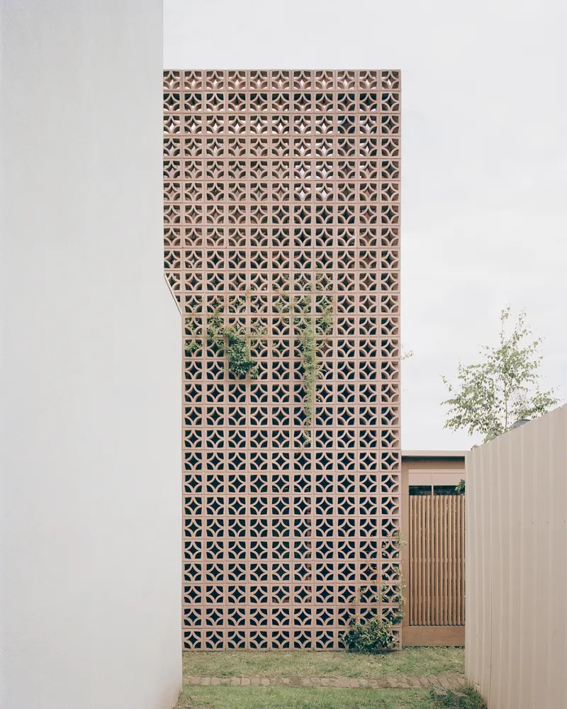 Street view of the geometric terracotta screen facade rising above a lawn and adjacent volumes