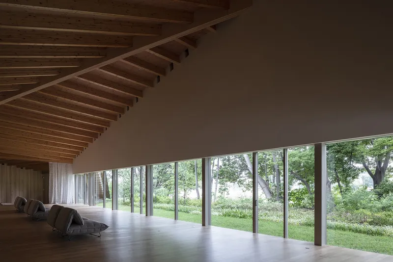 Interior gallery space with exposed timber ceiling beams and floor-to-ceiling windows overlooking gardens