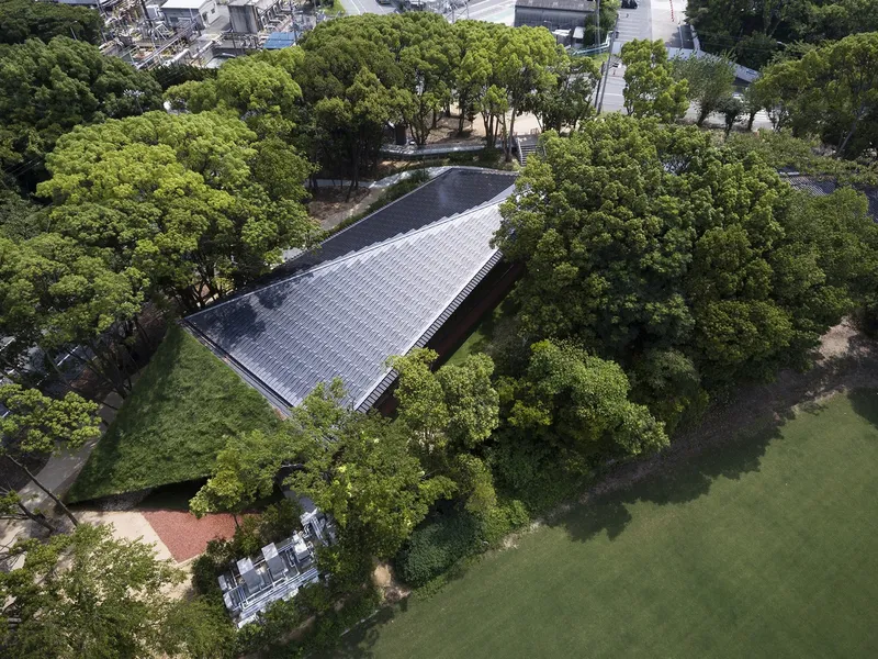 Aerial view of the linear tiled roof nestled among mature trees in parkland